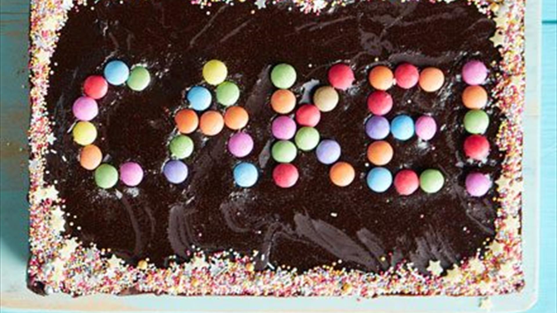 Image is of a cake with sweets spelling CAKE