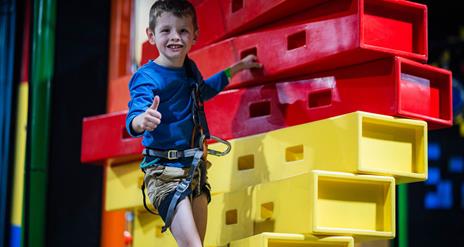 Boy in harness climbing up stacked blocks