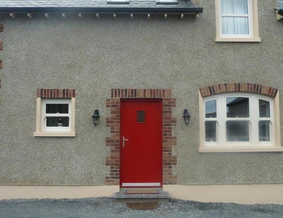 Image shows red front door of stone property with gravel drive