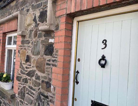 Image shows front door of property with flower beds on window sills