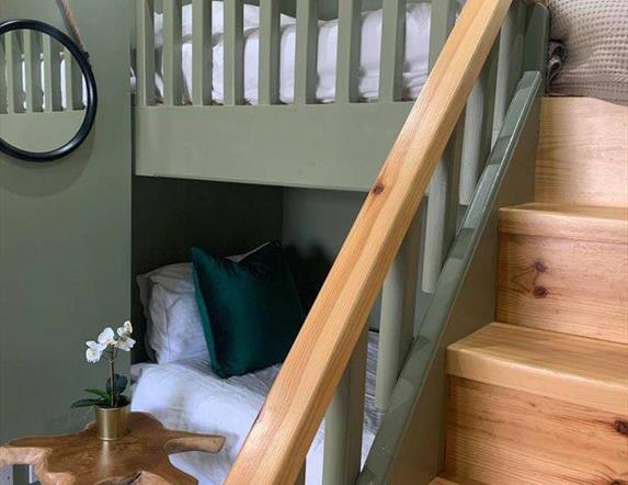 Image is of loft bedroom with bunk beds with wooden stairs up to top bunk