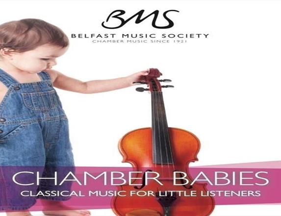 Image shows baby with blue dungarees and holding a violin.