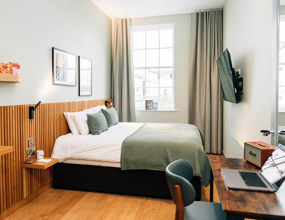 Image shows a double bed in a hotel room with paintings of Northern Ireland on the background wall