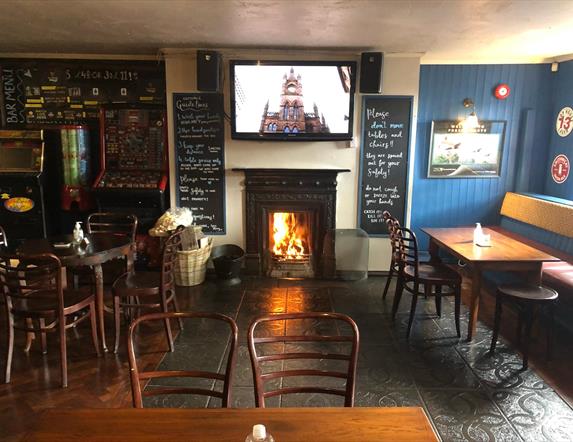 Image is of the lounge area of the bar with open fire blazing and table and chairs
