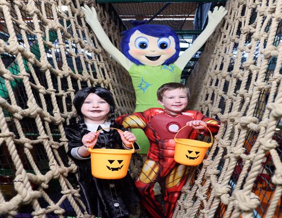 Image shows two children in halloween costume holding pumpkin buckets with a character behind them and all standing on the nets at Indiana Land