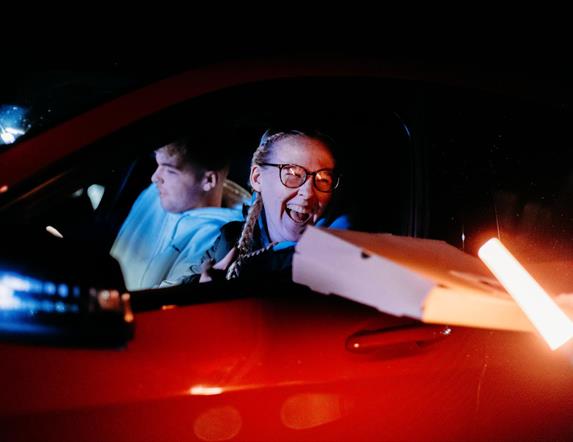 Image is of person holding pizza box in a car at Let's Go Hydro drive-in