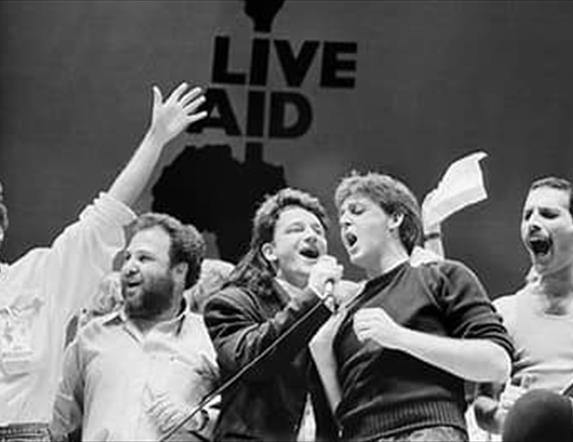 Image is of various rock stars performing on stage at Live Aid Wembley Arena London