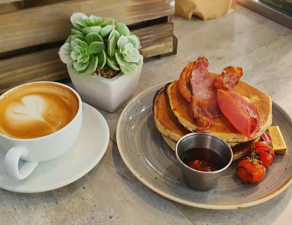 Image shows a cup of coffee and bacon with pancakes at Paul Hampton cafe