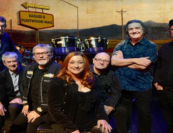Image shows The Illegals bandmates with drum set and Eagles and Fleetwood Mac sign in background.