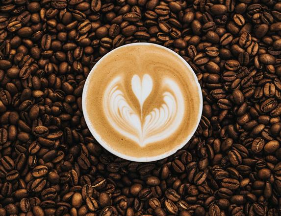 Image shows coffee beans and cup of coffee sitting in the middle.