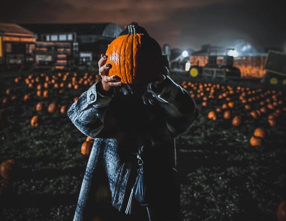 Woman holding up pumpkin in dark pumpkin patch at Streamvale Farm