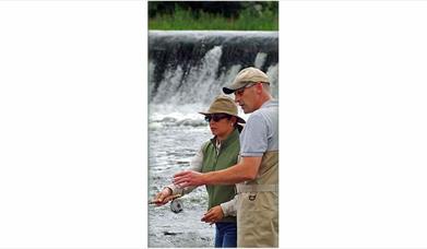 Image is of man showing woman how to fish