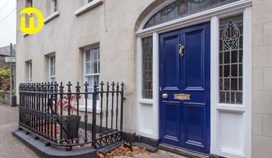 Image shows royal blue front door with iron railing to the left of the door Door leads out onto footpath on street