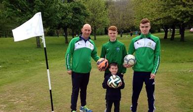 Image is adults and a child holding footballs on the golf course