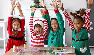 Image is of children dressed up for Christmas and doing arts and crafts