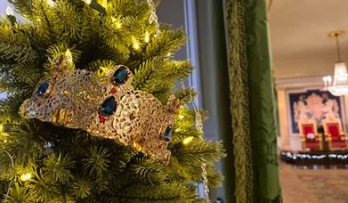 An image of a Christmas tree by the entrance to the Throne Room. The tree has lights and a gold crown with jewels.