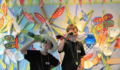 Two children playing with binoculars with art on the wall in the background