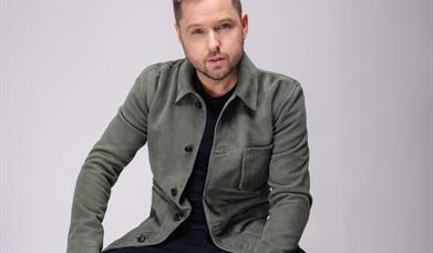 Image shows Derek Ryan sitting on stool.
