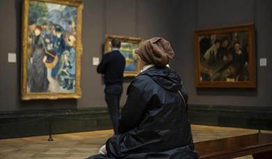 Picture of 2 people looking at works of art, one is sitting and one is standing
