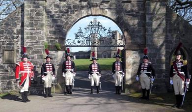 Image shows 7 guards in traditional dress outside the gates of Hillsborough Fort.