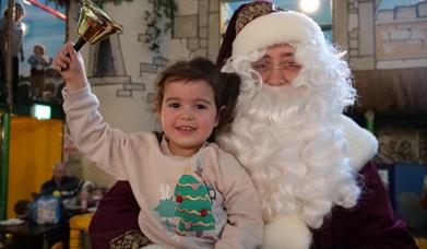 Pictured is Santa Claus with a Child ringing a bell.