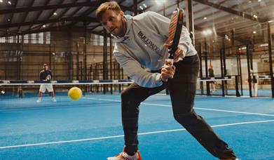 Image shows two individuals playing Padel Tennis on blue court.
