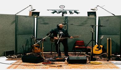 Image is of musician Andy White playing guitar in a recording studio