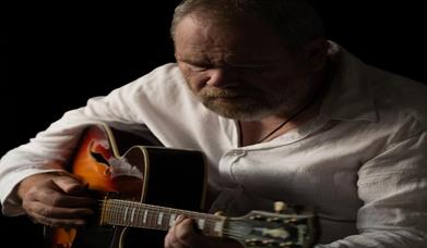 Image is of musician Ken Haddock playing acoustic guitar