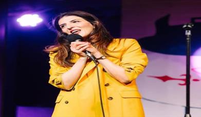 Image is of comedienne Wafa Daldoul on stage performing