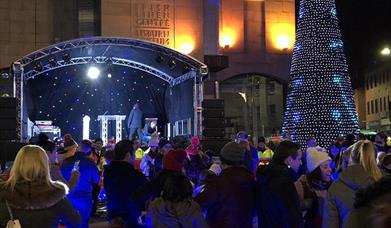 Persons gathered around the stage and Christmas tree