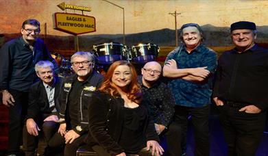 Image shows The Illegals bandmates with drum set and Eagles and Fleetwood Mac sign in background.