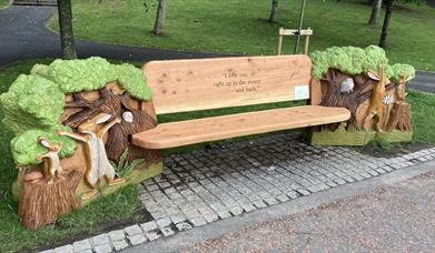 Image shows wooden bench in a park with engraving 'I Love you to the moon and back7