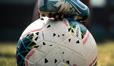 An image of a football with someone holding it in place by their football boot