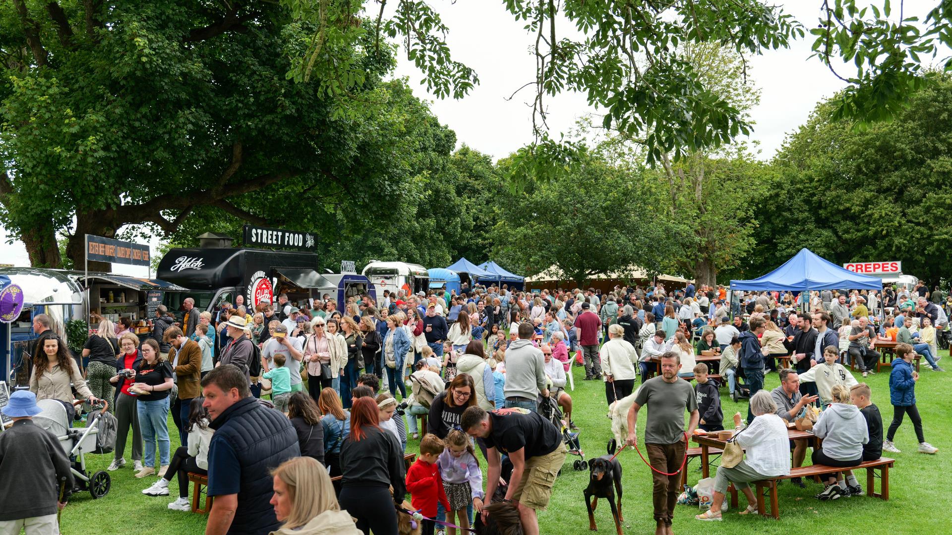 Large crowd at Moira Speciality Food Fair with market stalls, picnic tables, and trees in a park setting
