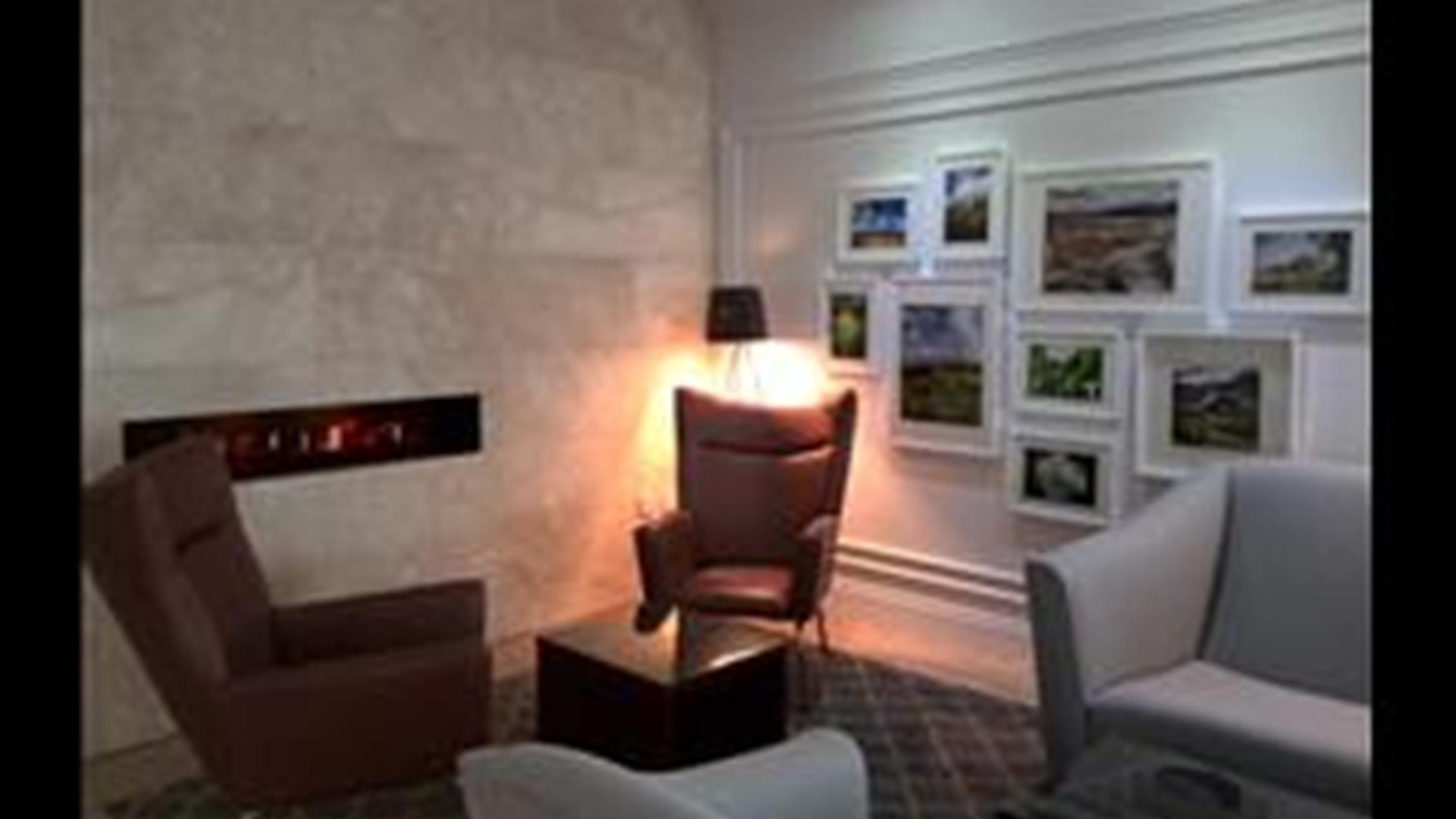 Image shows lounge area with chairs and various paintings on the wall
