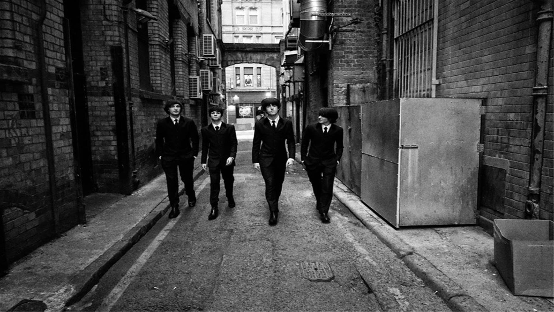 Black and White Image shows Beatles Tribute members in a alleyway dressed in suits.