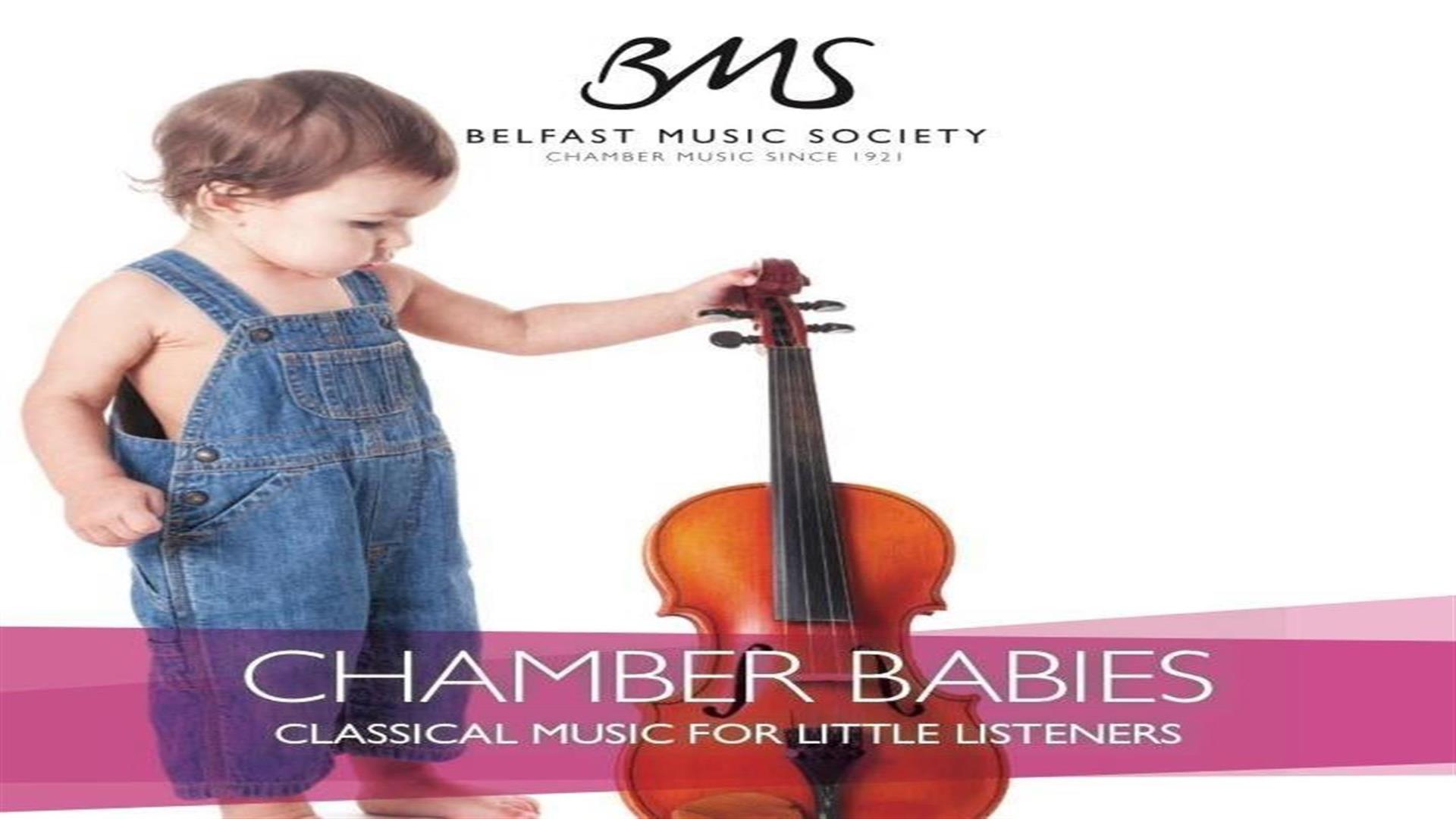 Image shows baby with blue dungarees and holding a violin.