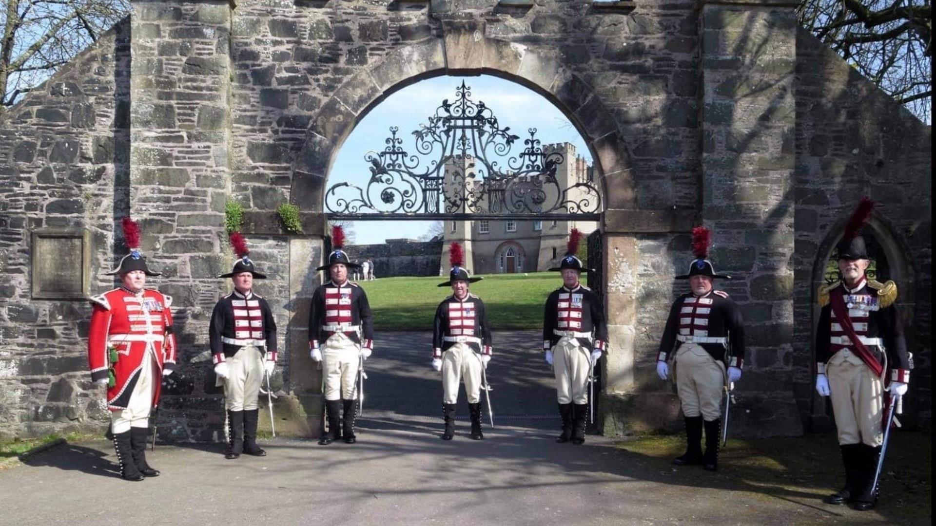 Image shows 7 guards in traditional dress outside the gates of Hillsborough Fort.