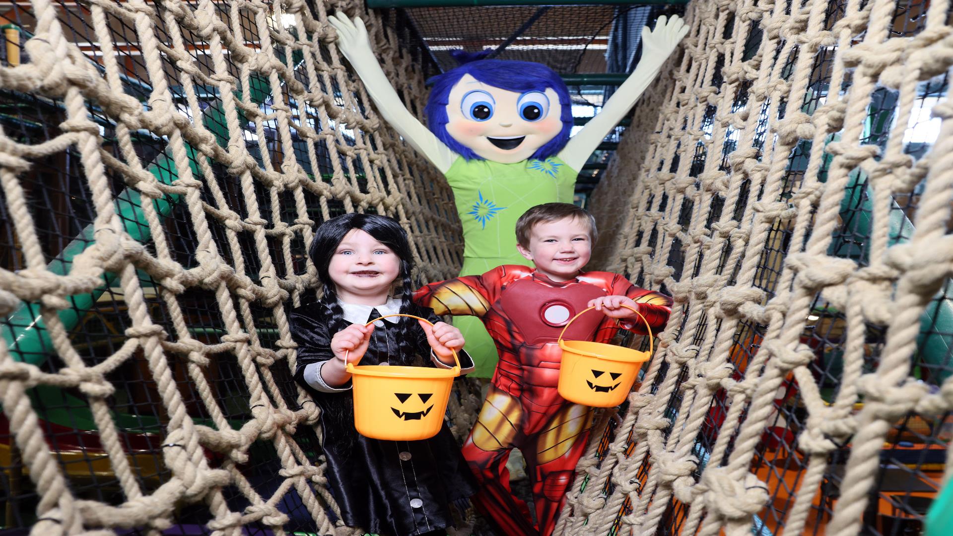 Image shows two children in halloween costume holding pumpkin buckets with a character behind them and all standing on the nets at Indiana Land
