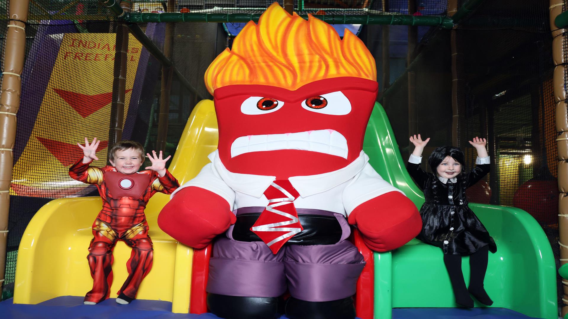 Image shows yellow and green sides at Indiana land with character positioned in the middle and two children sitting on each of the slides dressed in H