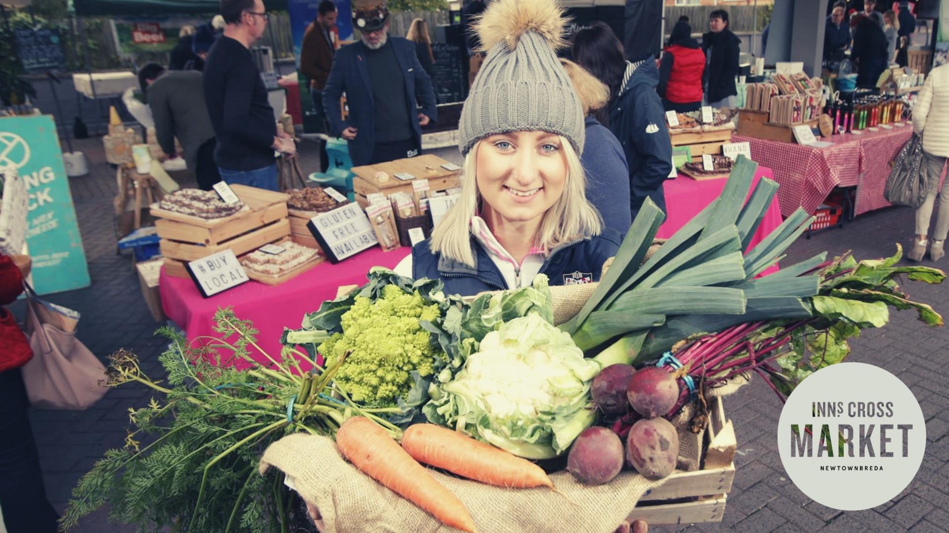 Image is of a trader holding a box of various vegetables at Inns Cross Market, Newtownbreda Belfast