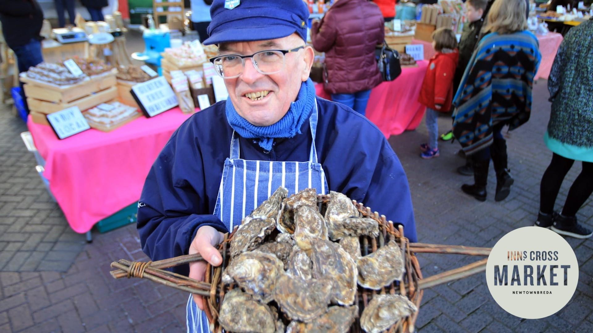 Image is of a trader holding a plate of oysters at the Inns Cross Market in Newtownbreda Belfast