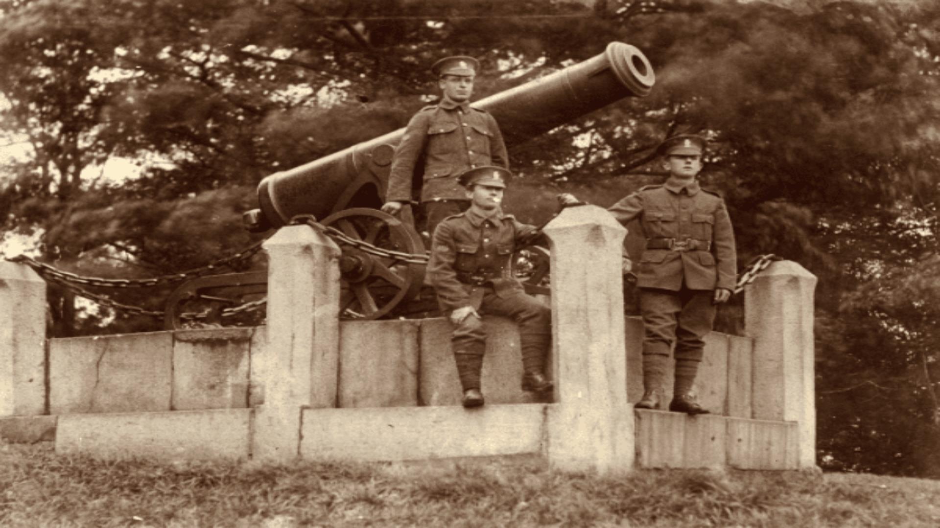 Black and white Image of 3 soldiers dressed in uniform in front of cannon.
