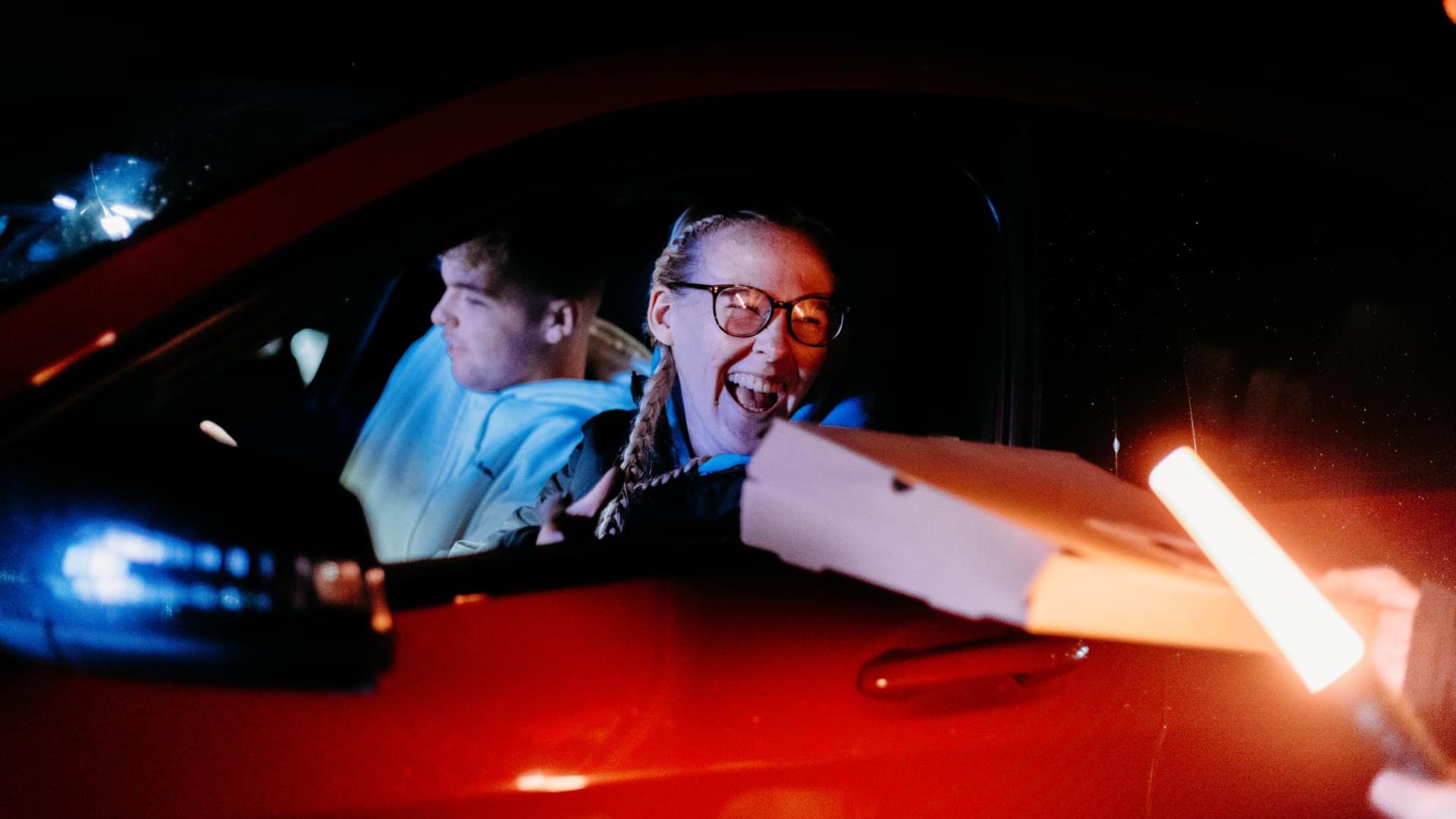 Image is of person holding pizza box in a car at Let's Go Hydro drive-in