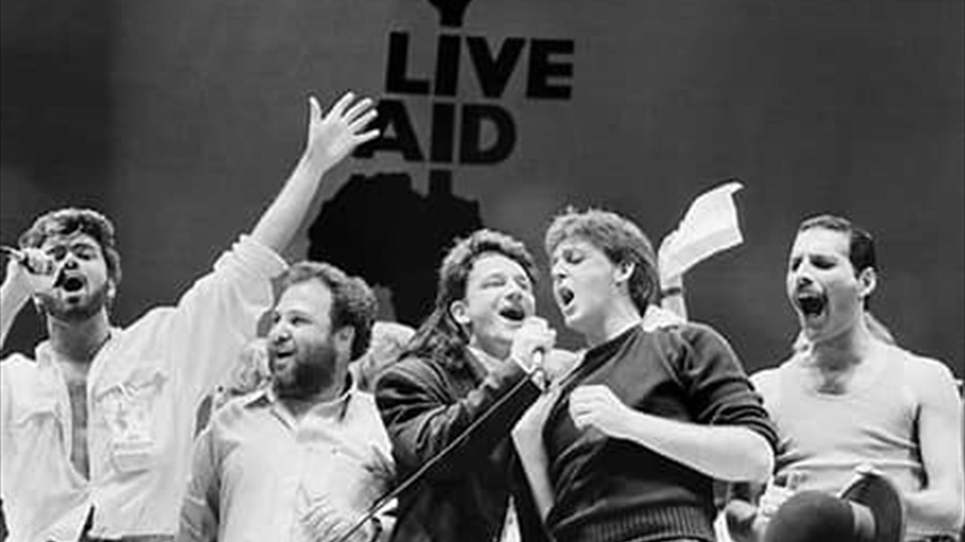 Image is of various rock stars performing on stage at Live Aid Wembley Arena London