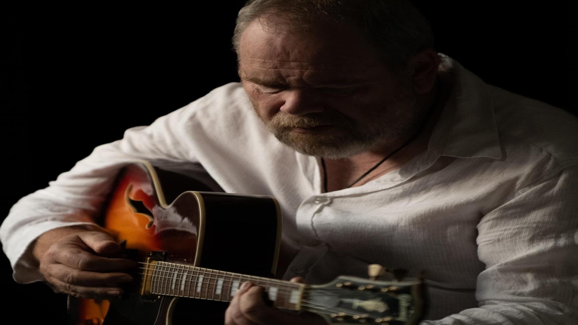 Image is of musician Ken Haddock playing acoustic guitar