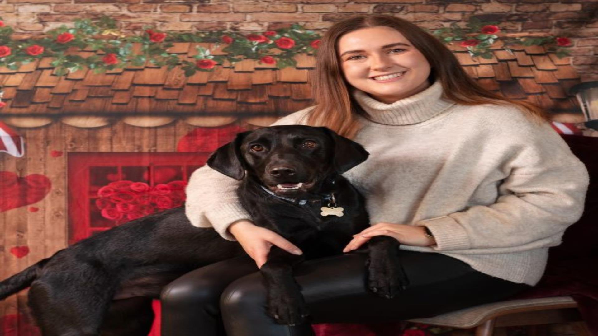 Image is of a woman with a black dog sitting on her knee