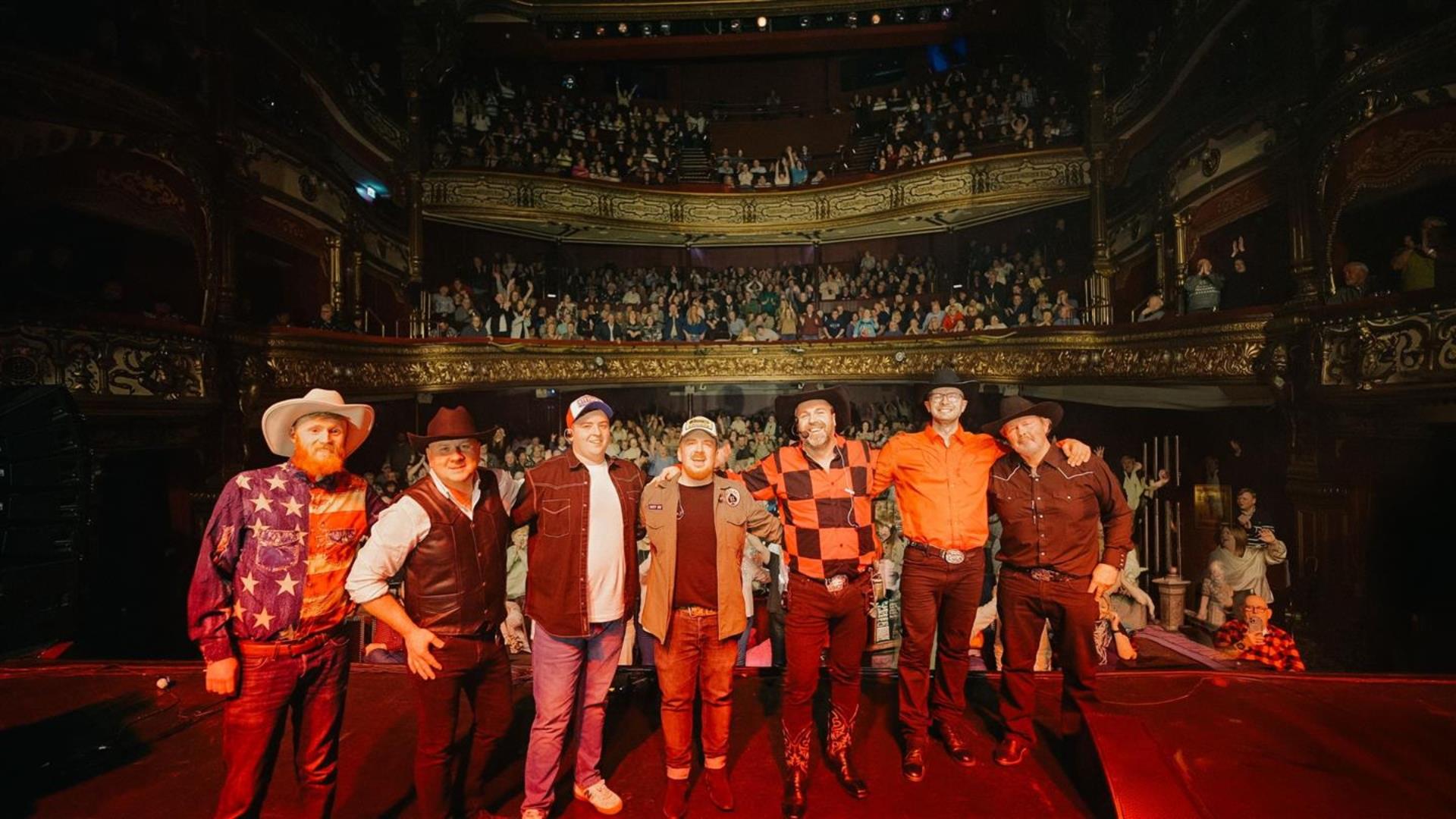 Image is of the members of Garth Brooks tribute band Thunder Rolls on stage with a packed audience behind them