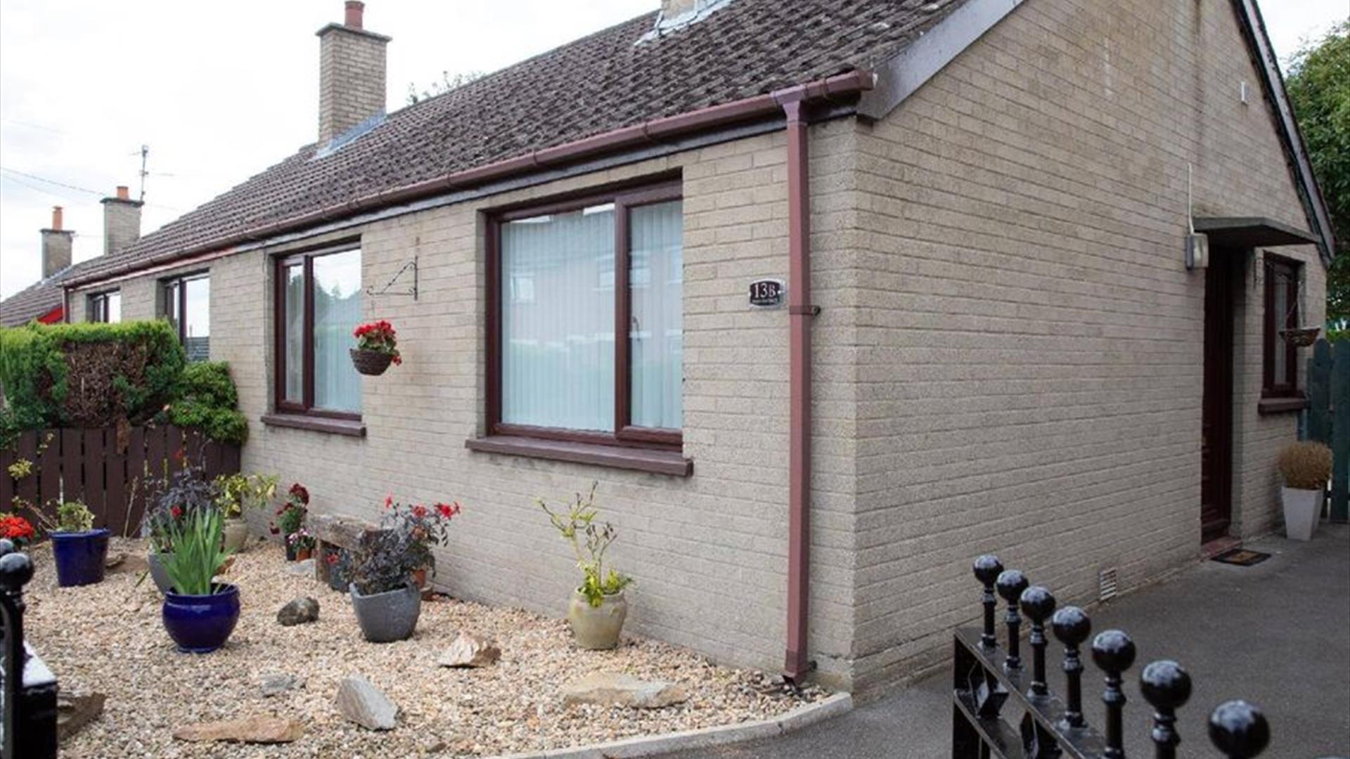An Image of the front of the semi-detached bungalow with driveway to the side and set of gates.