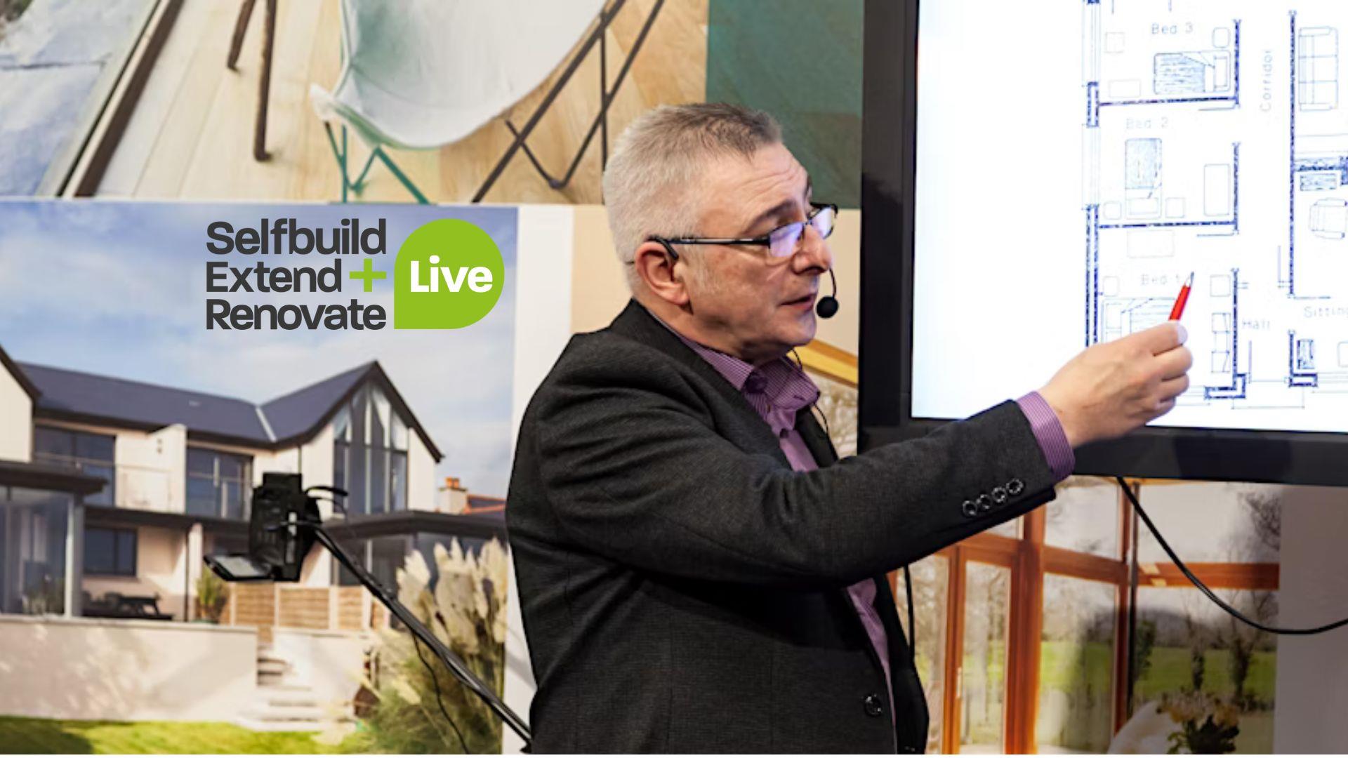 Image is of exhibitor pointing at a set of house plans at the Selfbuild Extend Renovate exhibition in Eikon Exhibition Centre Lisburn